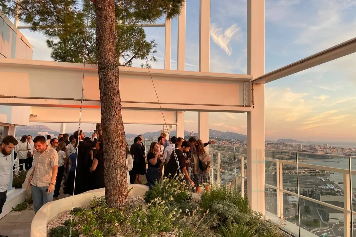 Un groupe de personnes se mêlant à une réunion en plein air, entouré de plantes et d'architecture, avec un arrière-plan montagneux.