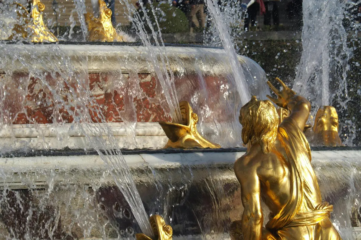 Une fontaine décorative avec des statues en or et des jets d'eau, avec une sculpture détaillée d'un personnage au premier plan.