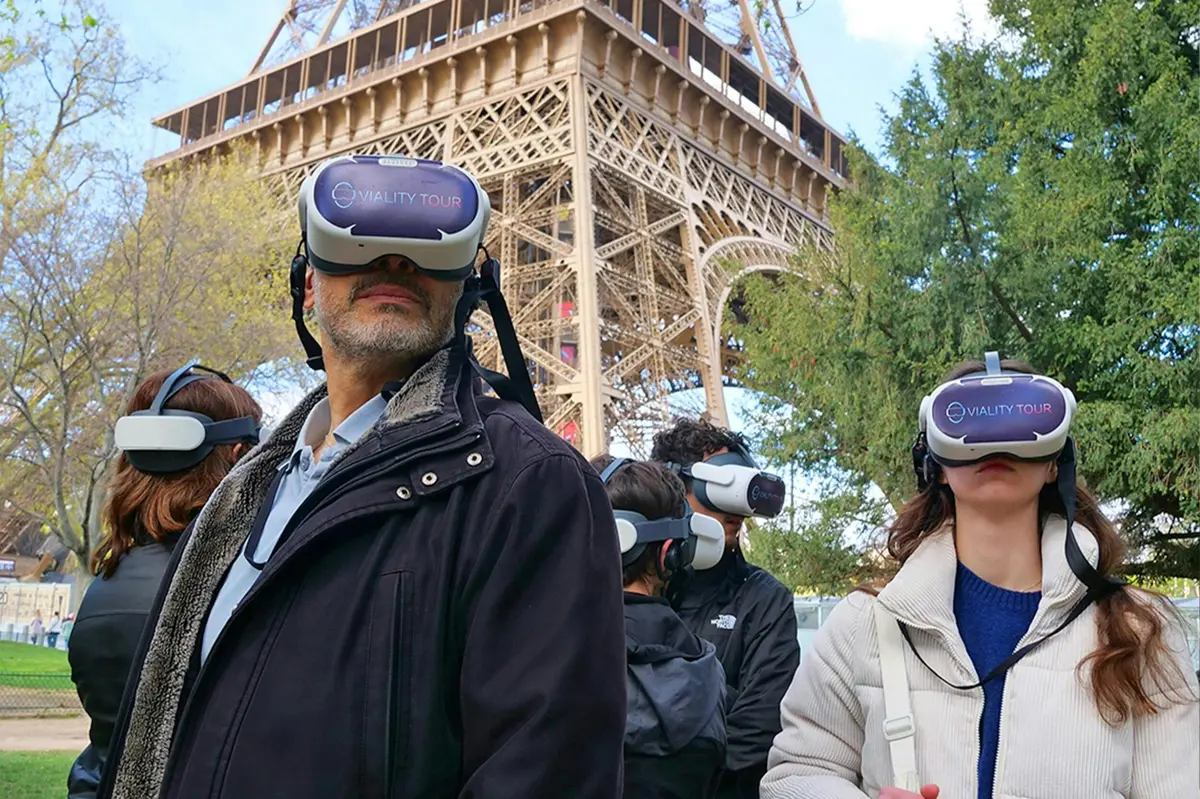 Un groupe de personnes portant des casques de réalité virtuelle portant l'inscription « Viality Tour » se tient près de la Tour Eiffel et de quelques arbres.