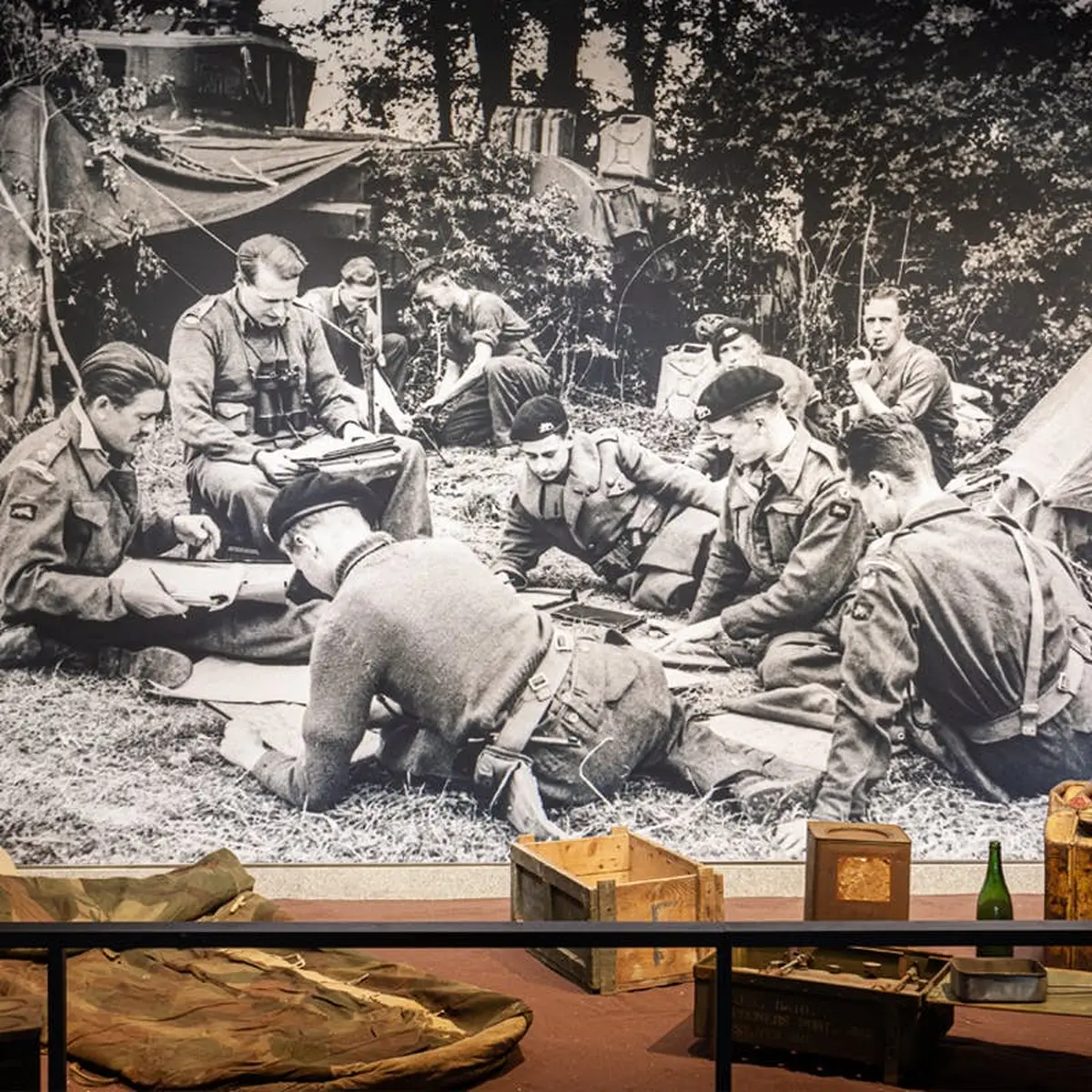 Photo en noir et blanc de soldats dans un campement, avec au premier plan du matériel et des caisses.