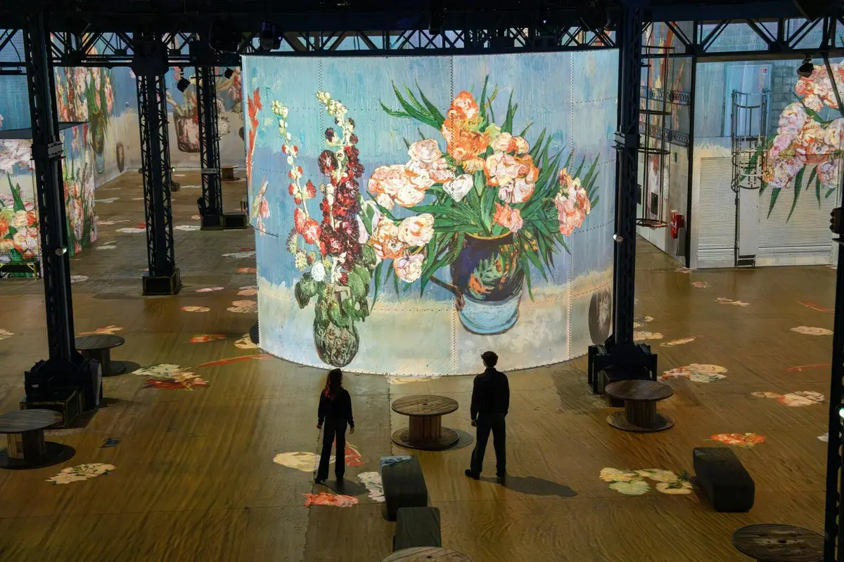 Deux personnes se tiennent dans une grande pièce où est projetée, sur un écran cylindrique, une peinture florale aux couleurs vives.