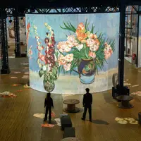 Deux personnes se tiennent dans une grande pièce où est projetée, sur un écran cylindrique, une peinture florale aux couleurs vives. &copy; Culturespaces___Cyrille_de_la_Motte_Rouge