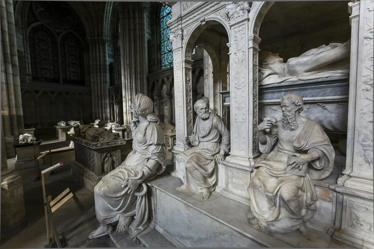 Statues en marbre de personnages assis dans une cathédrale historique, avec des détails complexes et des structures arquées en arrière-plan.