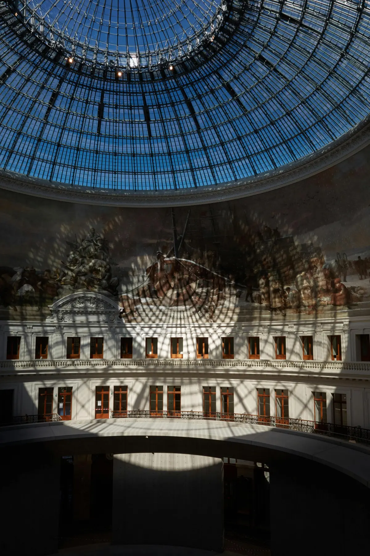 Un atrium à dôme de verre avec une grande peinture murale et de multiples fenêtres, qui projettent des ombres complexes sur les murs.