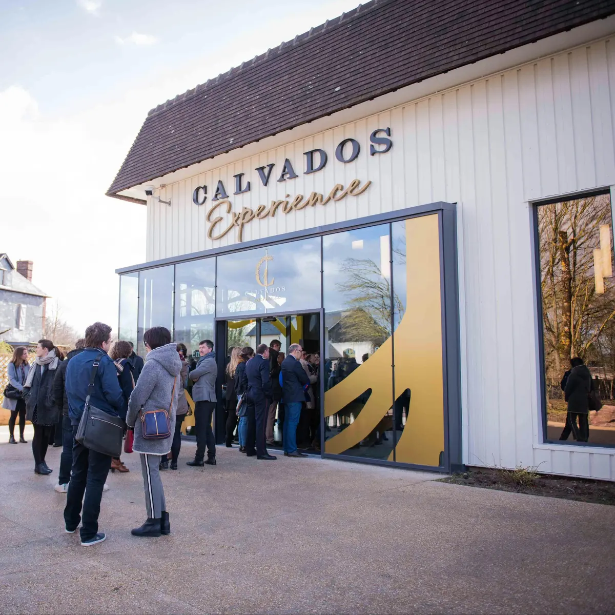Des personnes se sont rassemblées devant l'entrée d'un bâtiment sur lequel on pouvait lire en grosses lettres Calvados Experience.