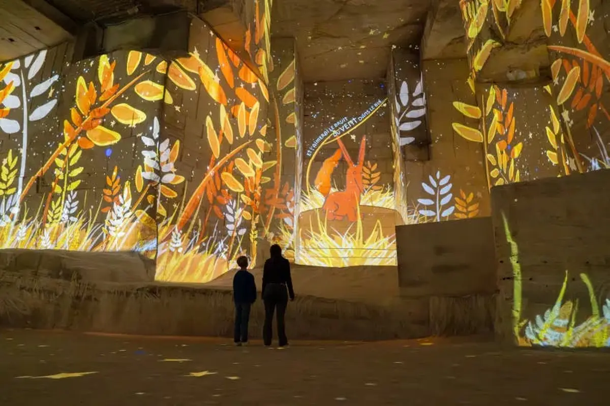 Deux personnes se tiennent dans un grand espace éclairé où sont projetées des images de feuilles orange et jaunes et d'un personnage ressemblant à un lapin.