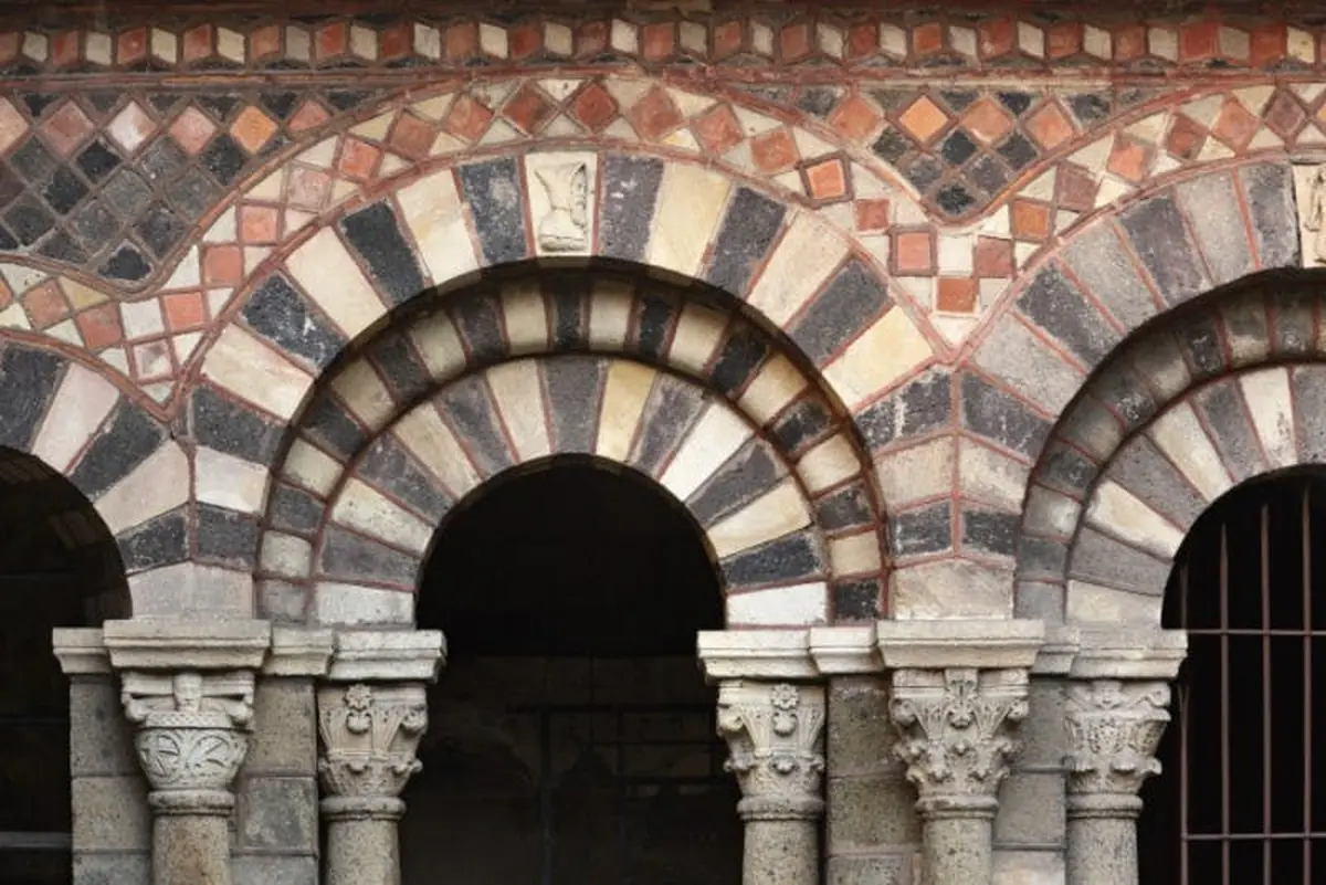 Porte arquée en pierre avec des pierres noires et blanches alternées, des colonnes décoratives et un motif de mosaïque détaillé au-dessus.