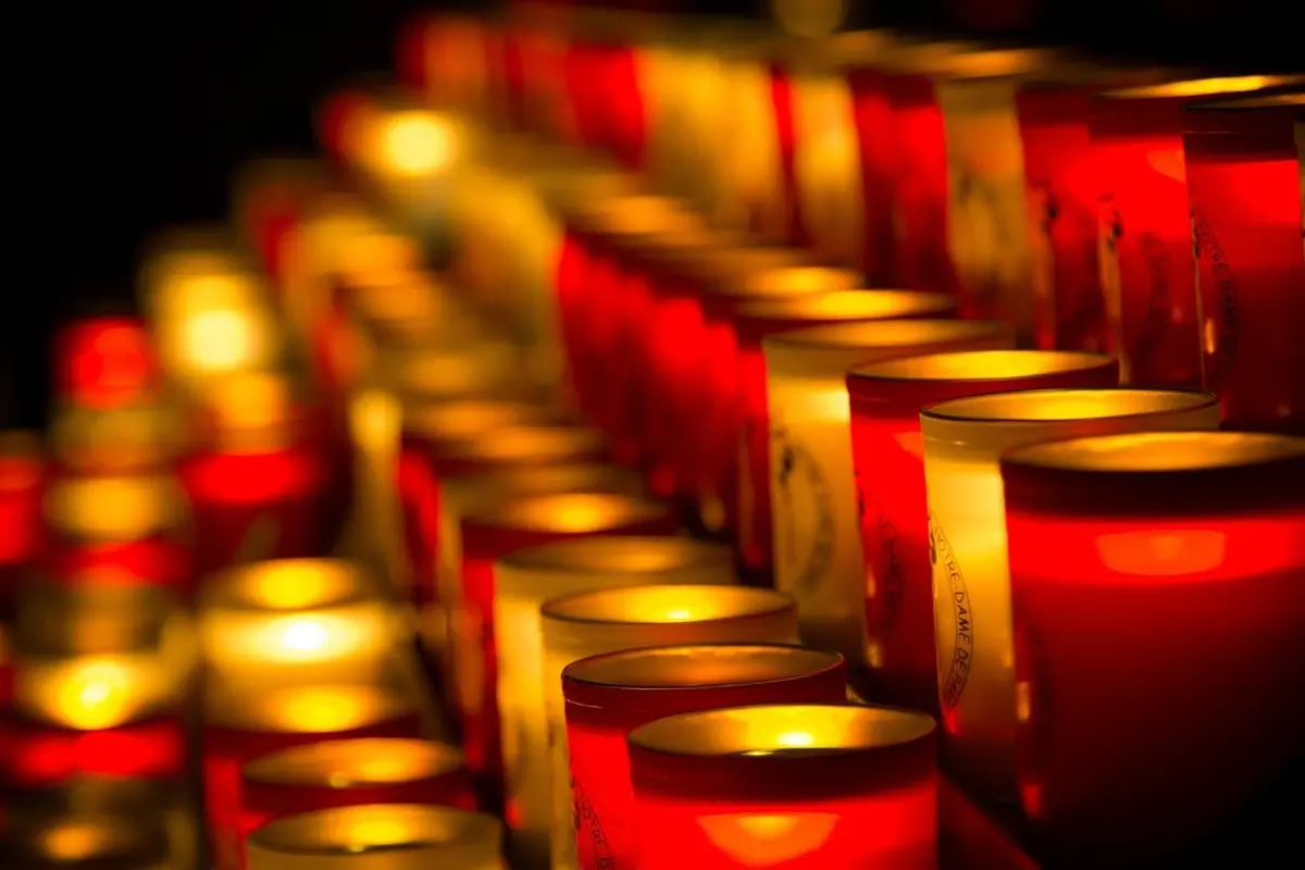 Des rangées de bougies rouges et blanches brillent dans l'obscurité.