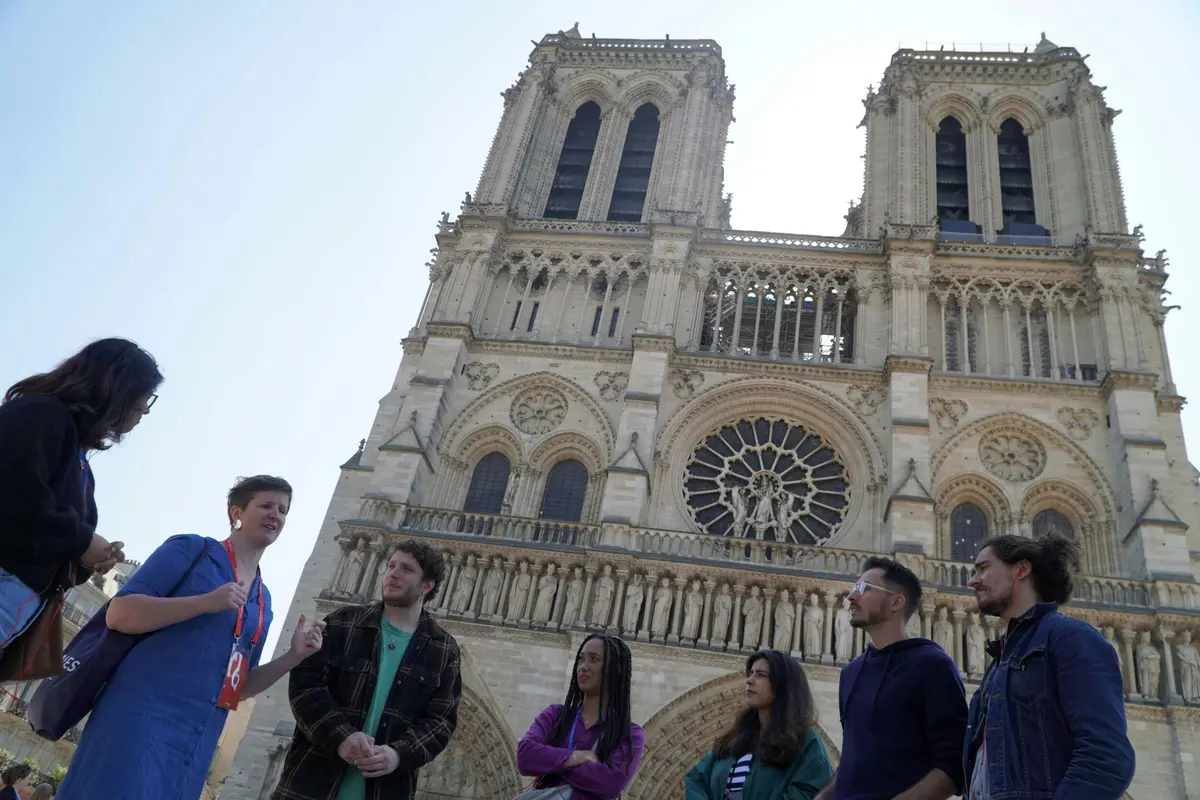Un guide s'adresse à quatre personnes devant la cathédrale Notre-Dame par temps clair.