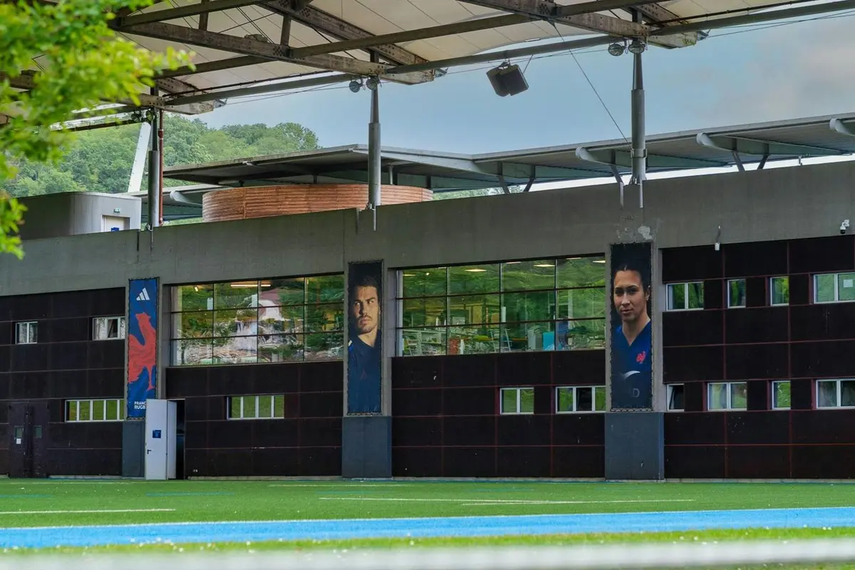 Un bâtiment sur la façade duquel sont exposés de grands portraits de deux personnes, situé près d'un terrain de sport en gazon synthétique.