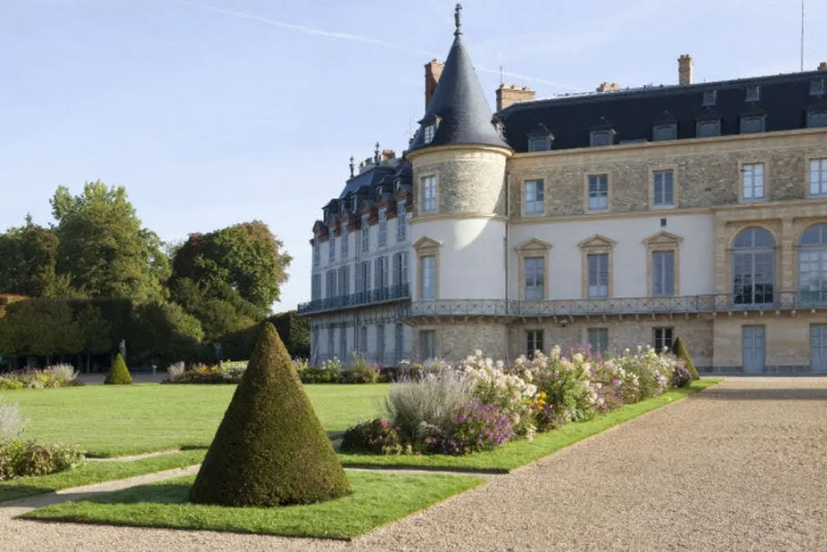 Un château majestueux avec une tour conique, des jardins soignés et un chemin de gravier par temps clair.