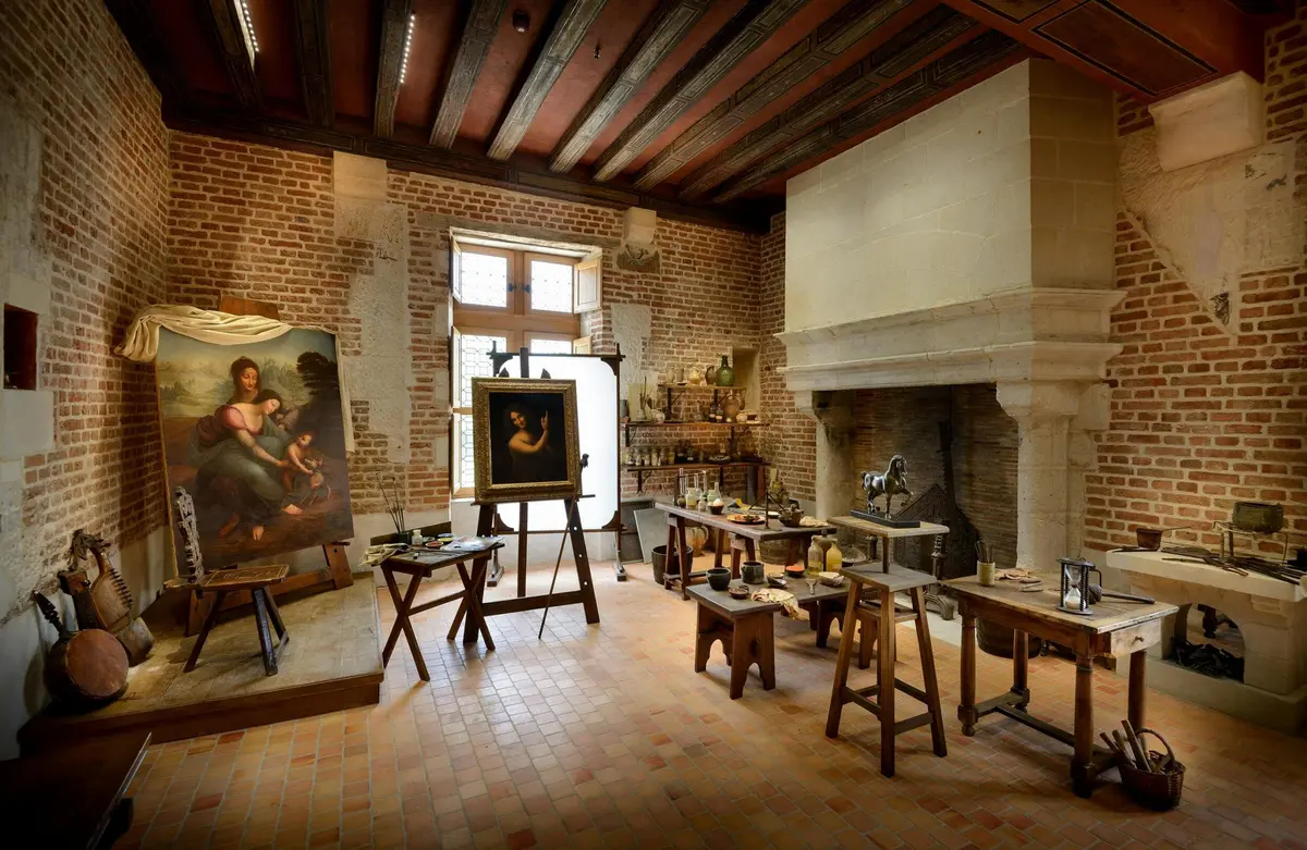 Un studio d'artiste rustique avec des tableaux sur des chevalets, des meubles en bois, une grande cheminée et du matériel d'art sur des tables.