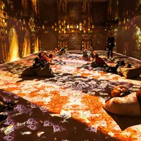 Une salle avec des projections numériques immersives sur les murs et le sol, représentant des motifs vibrants, et des personnes assises sur des coussins. &copy; ®Cités Immersives