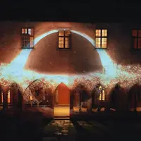 Vue nocturne d'un bâtiment aux fenêtres cintrées, éclairé par une projection lumineuse formant un arc lumineux et des particules. &copy; Musée Unterlinden