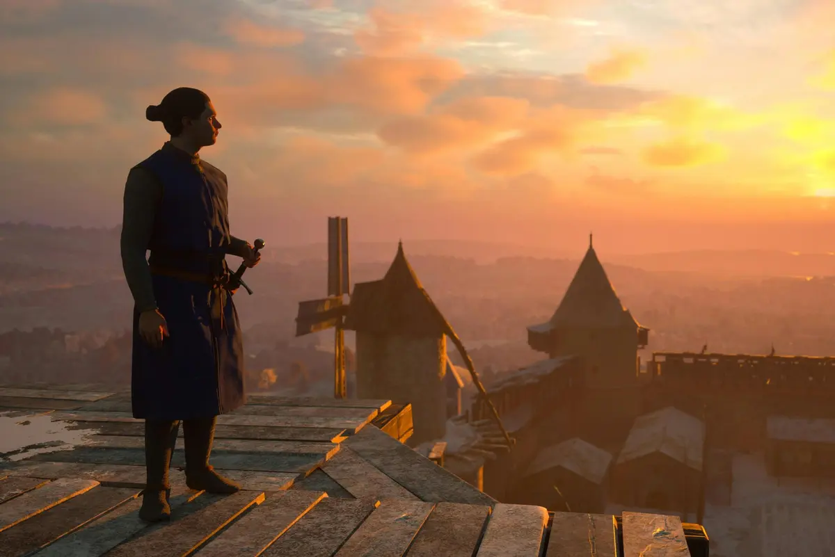 Une personne en tenue médiévale se tient sur un toit au coucher du soleil, avec vue sur un château et un paysage lointain.