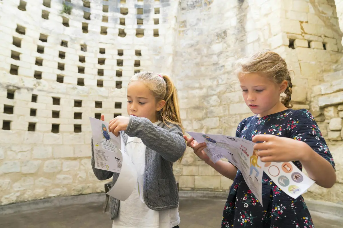 Deux jeunes filles examinent des papiers avec des dessins, debout devant un vieux mur de pierre.