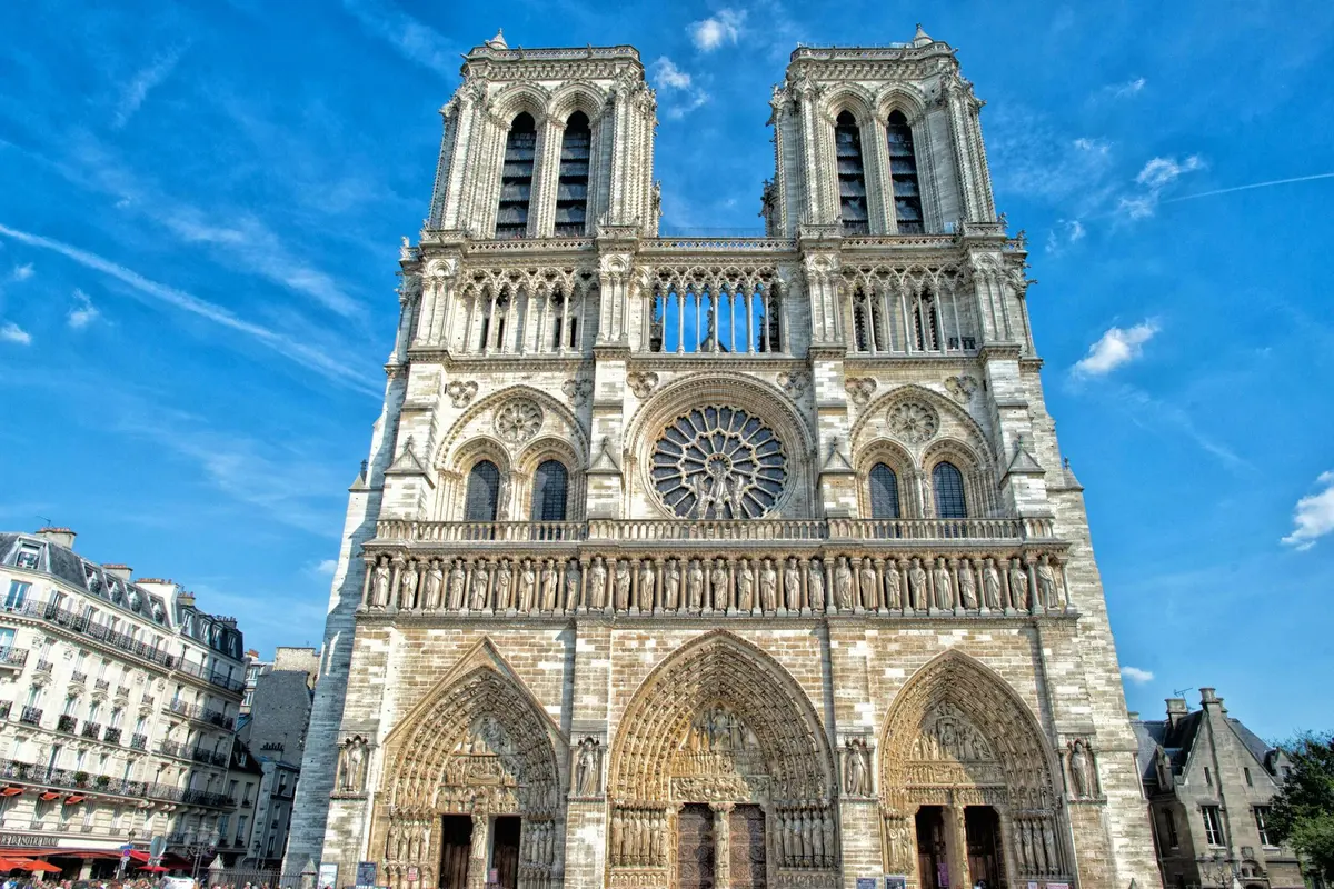 Vue de face de la cathédrale Notre-Dame de Paris par temps clair, avec ses tours jumelles, sa rosace et ses trois arcades.