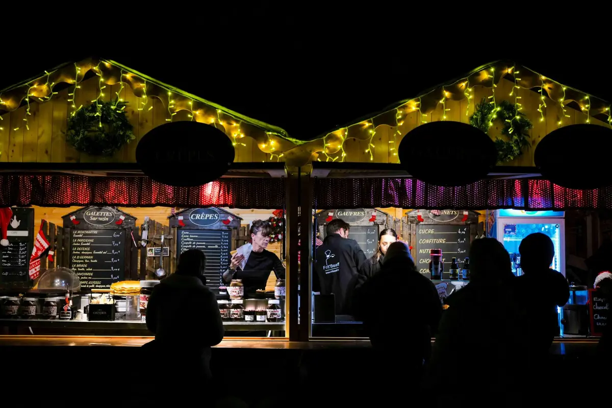 Deux stands de nourriture éclairés la nuit, avec des gens qui commandent, l'un étiqueté Crêpes et l'autre vendant diverses garnitures.