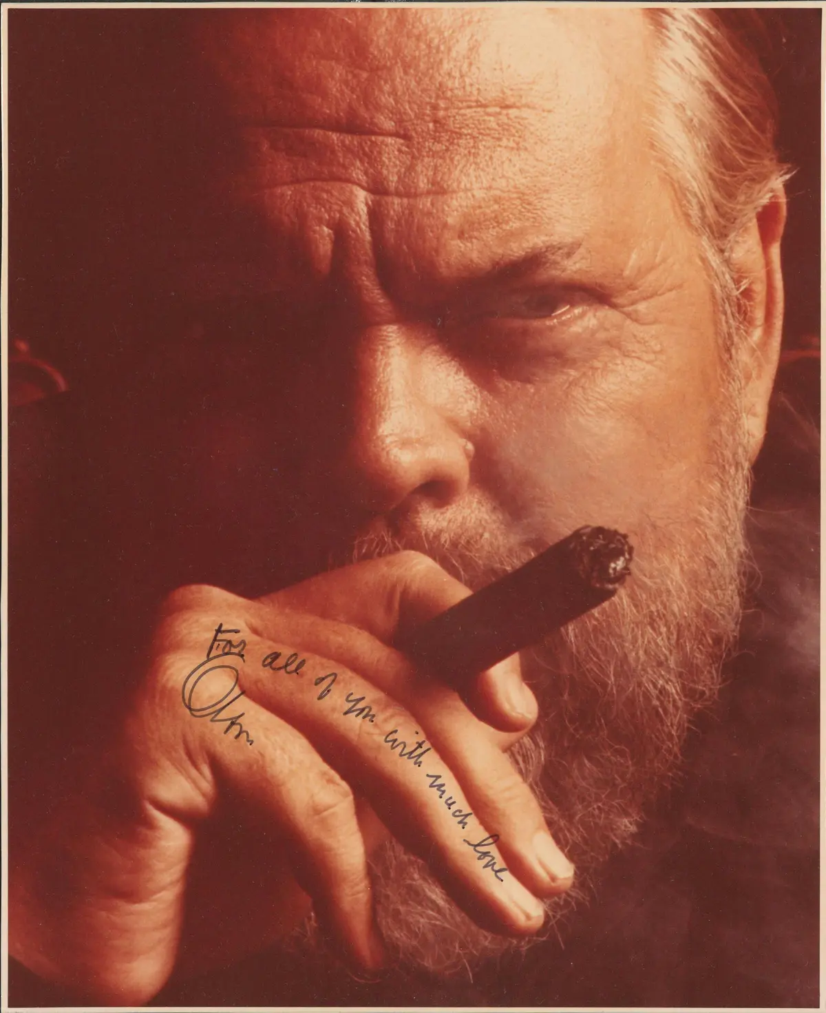 Un homme barbu à l'expression sérieuse fume un cigare, un message manuscrit sur la main.