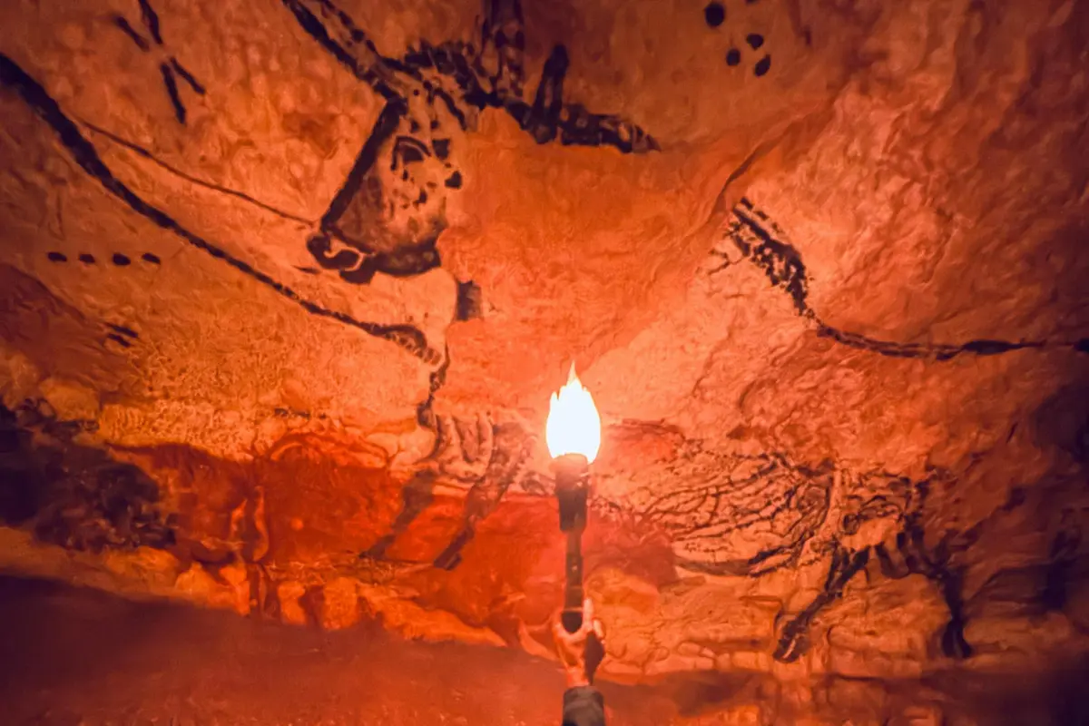 Une main tenant une torche éclaire des peintures rupestres préhistoriques d'animaux sur une surface rocheuse texturée.