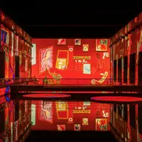 Une installation artistique colorée avec des murs rouge vif affichant diverses peintures, qui se reflètent sur un sol noir brillant. &copy; @Culturespaces / Geoffroy Groult