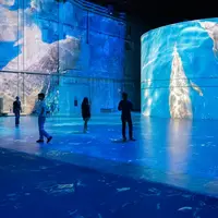 Des personnes debout dans une grande salle avec des projections bleues du sol au plafond créant un environnement sous-marin immersif. &copy; © Cultuirespaces