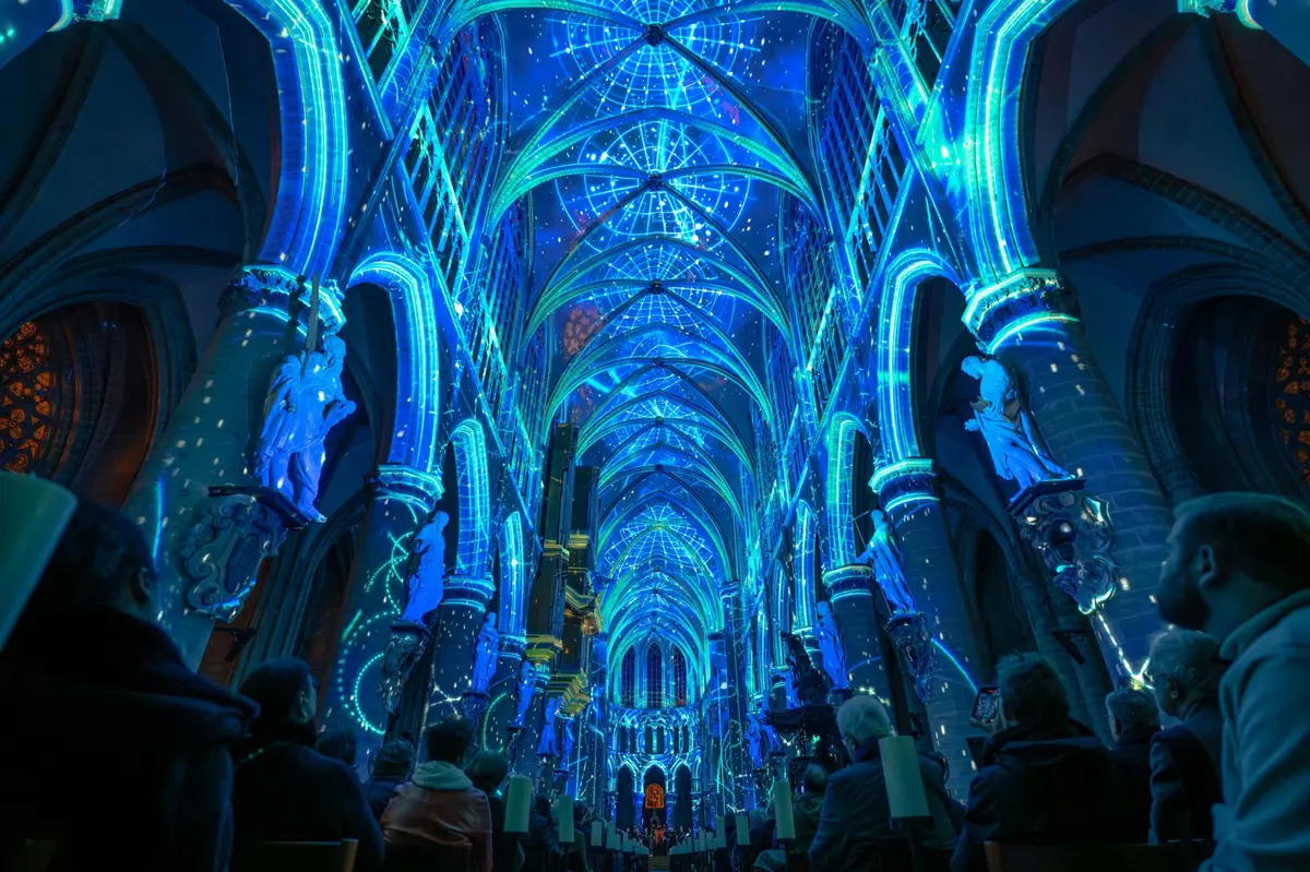Intérieur d'une cathédrale éclairé par des lumières bleues et vertes qui projettent des motifs géométriques et célestes sur le plafond.