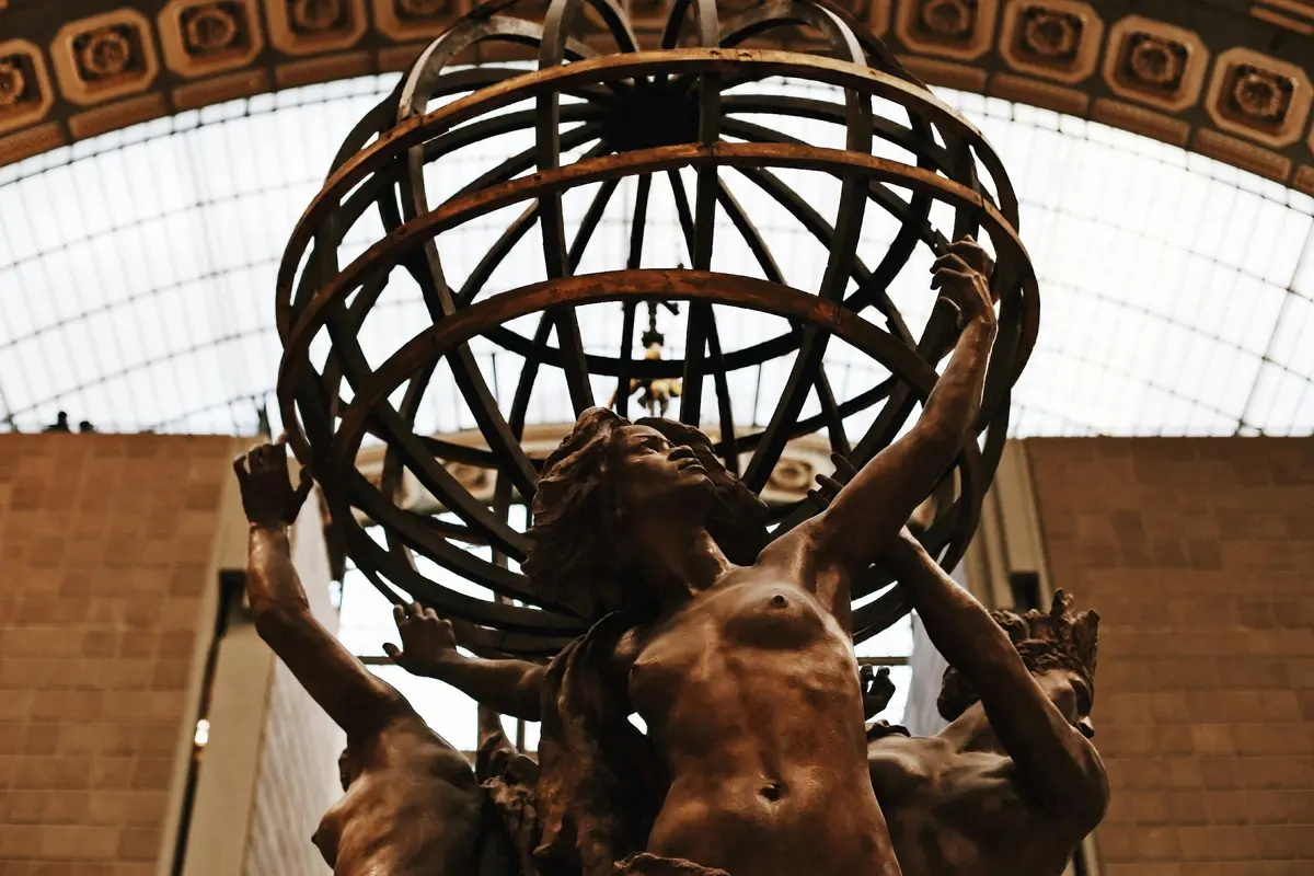 Statue en bronze d'une femme aux bras levés, entourée d'une structure métallique en forme de globe, située dans un bâtiment avec un toit en verre.