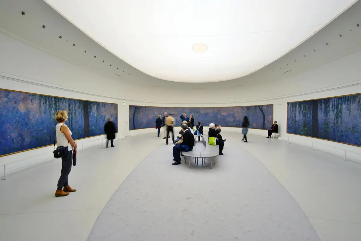 Des personnes observent de grandes peintures impressionnistes dans une salle de galerie incurvée avec des sièges au centre et un plafond en forme de dôme.
