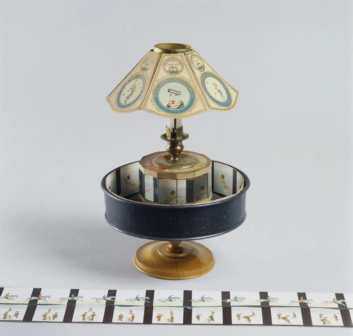 Un zoetrope vintage sur un support avec des bandes de papier illustrées montrant une séquence d'images, probablement pour créer des visuels animés.