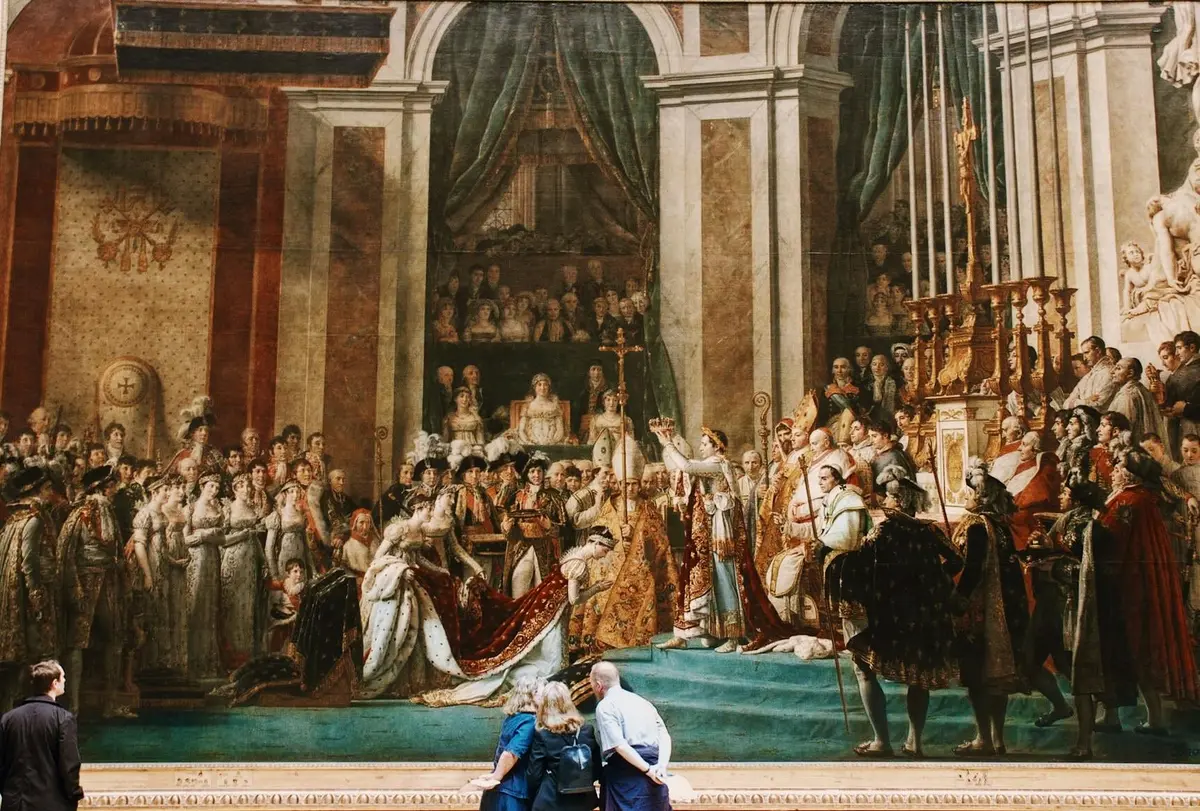Des personnes observent une grande peinture ornée représentant une scène historique de couronnement royal à l'intérieur d'une grande salle.