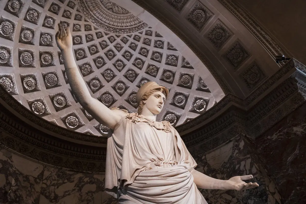 A marble statue of a robed figure with an arm raised, set against an ornate domed ceiling with intricate geometric patterns.