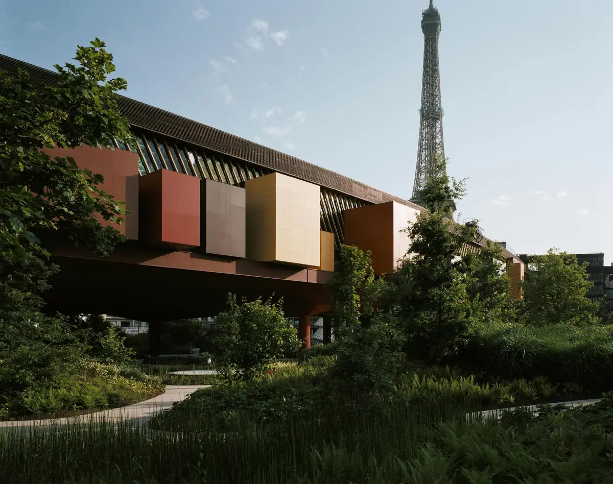 Bâtiment moderne avec de grandes structures cubiques colorées, entouré d'une végétation luxuriante, avec la Tour Eiffel en arrière-plan.