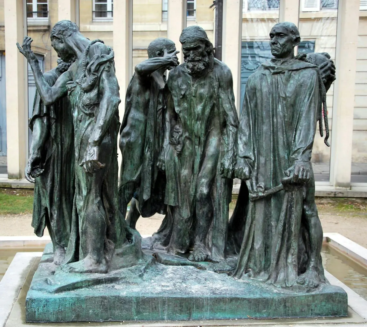 Une statue en bronze représente un groupe de six hommes solennels, dont certains ont la tête inclinée et d'autres le regard solennel, dans un cadre urbain en plein air.