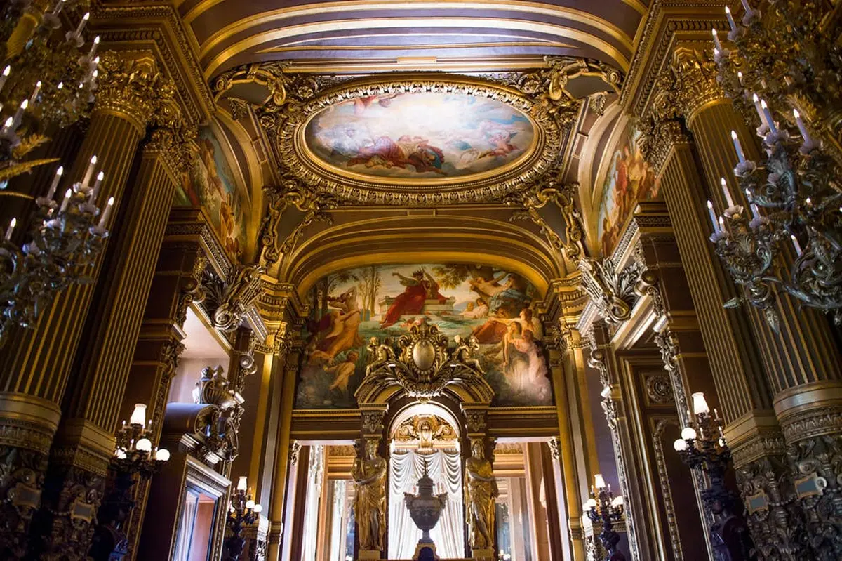 Une salle ornée de peintures détaillées au plafond et sur les murs, de décorations dorées élaborées et de lustres.