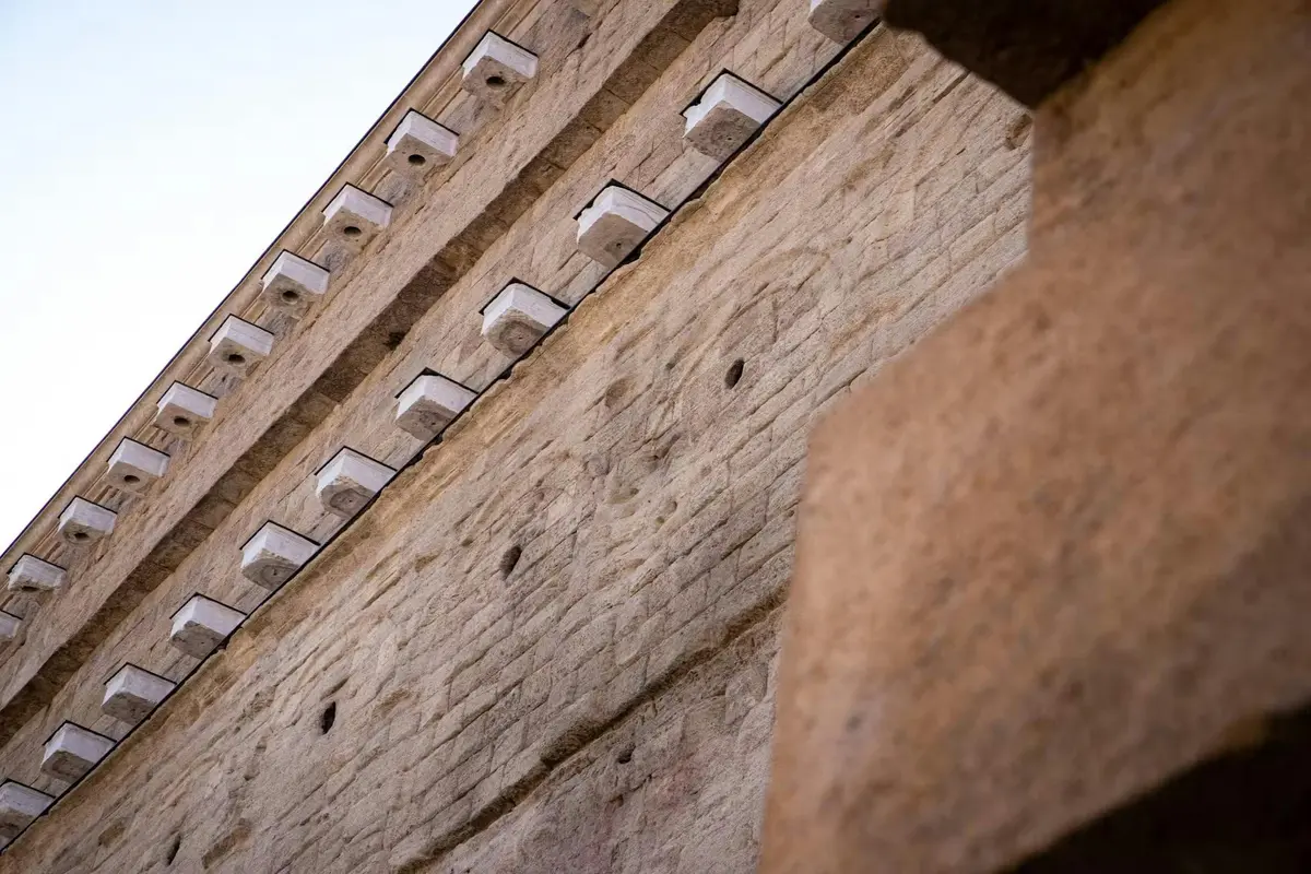 Gros plan d'un mur de pierre avec de multiples éléments de pierre blanche en saillie et des fils noirs, vu en contre-plongée sur le ciel.