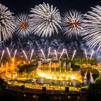 Un feu d'artifice vibrant au-dessus d'un spectacle aquatique nocturne en plein air, avec des fontaines et des structures illuminées. DR
