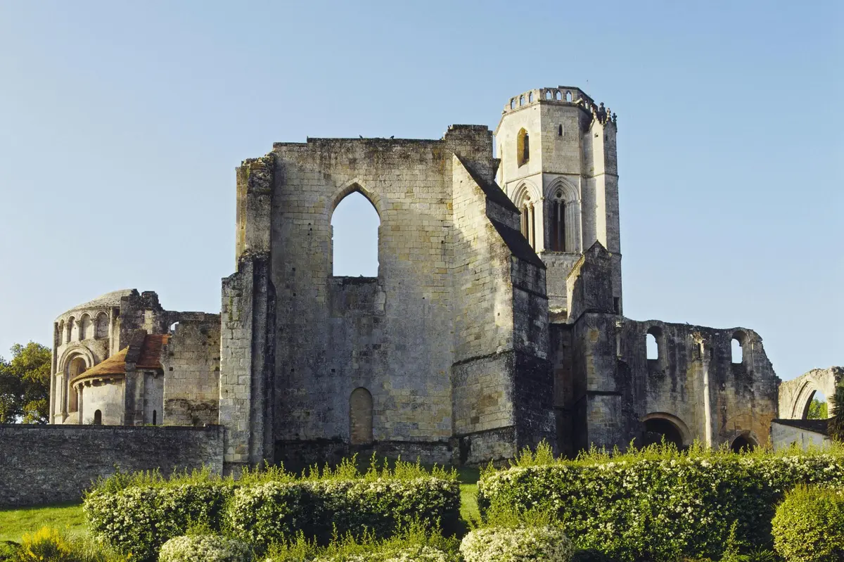 Anciennes ruines en pierre avec une tour et des fenêtres cintrées, entourées de verdure sous un ciel bleu clair.