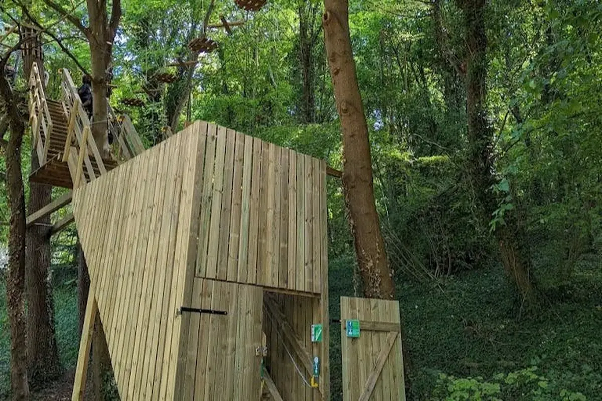Structures et plates-formes en bois dans une forêt, avec un parcours de cordes entre les arbres. La zone est entourée d'une végétation dense.