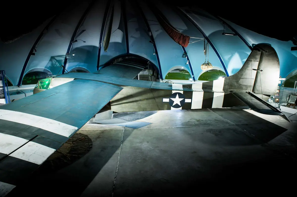 Une queue d'avion d'époque est exposée sous une structure bleue en forme d'arche, avec un éclairage doux qui met en valeur le décor sur le thème de l'aviation.