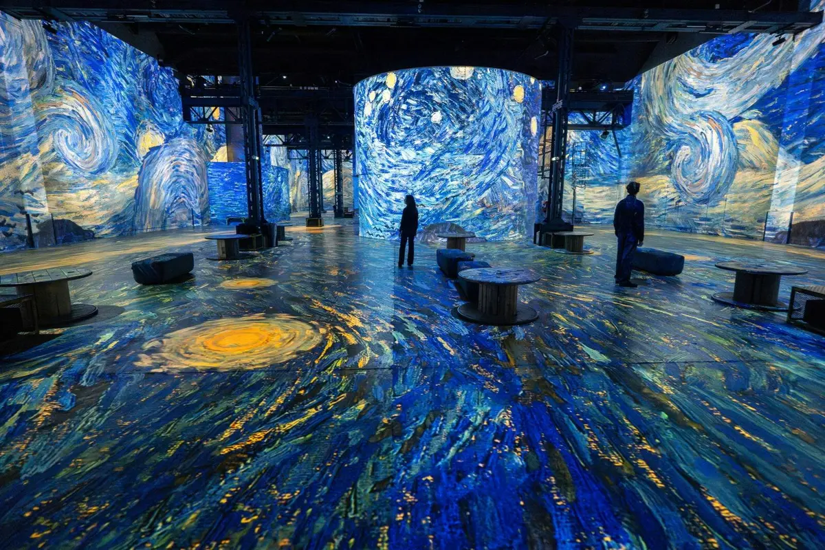 Des visiteurs se trouvent dans une exposition d'art immersive où « La Nuit étoilée » de Van Gogh est projetée sur les murs et le sol.