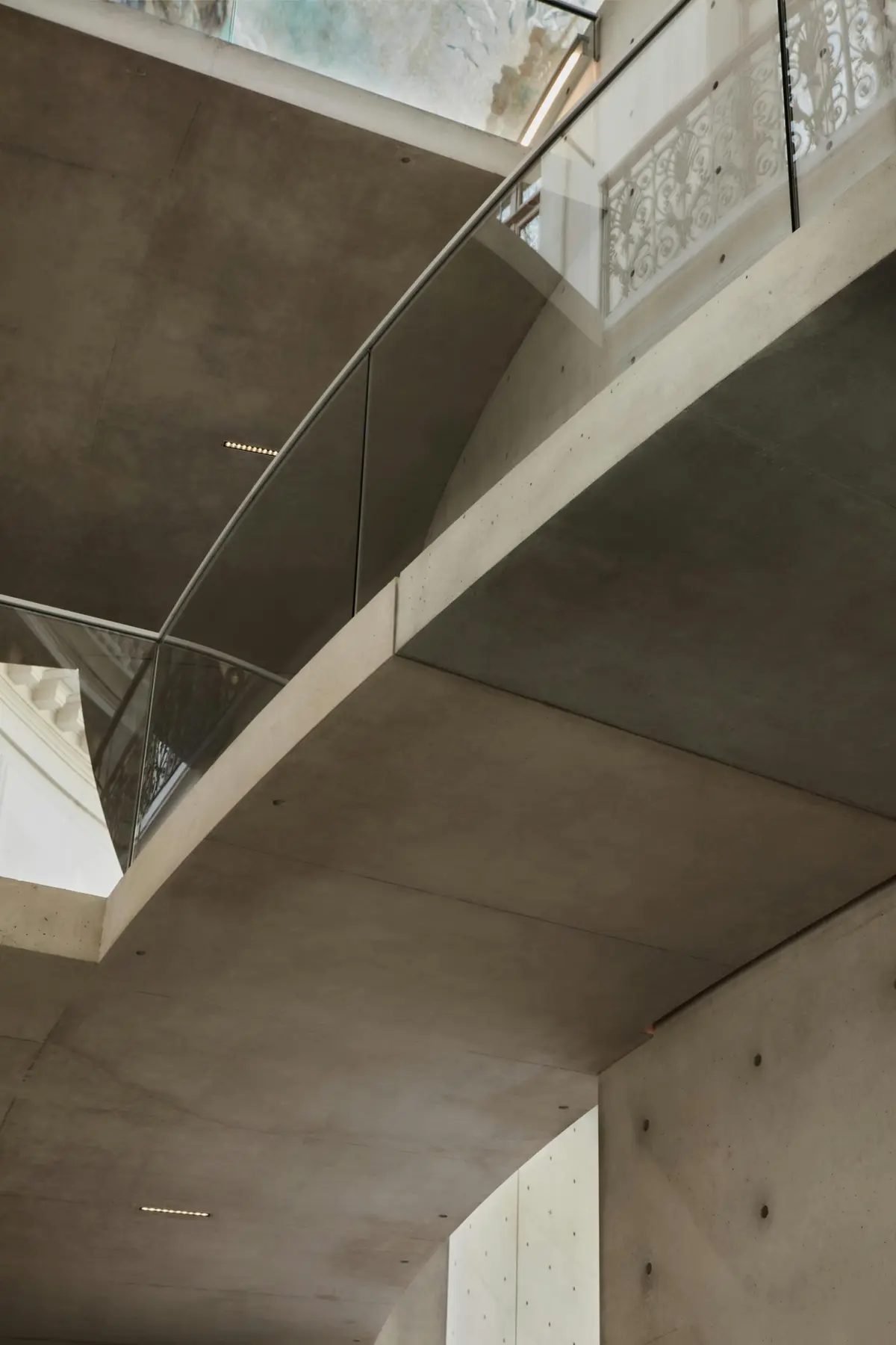 Intérieur moderne avec murs et plafond en béton, garde-corps en verre et supports métalliques vus de dessous.