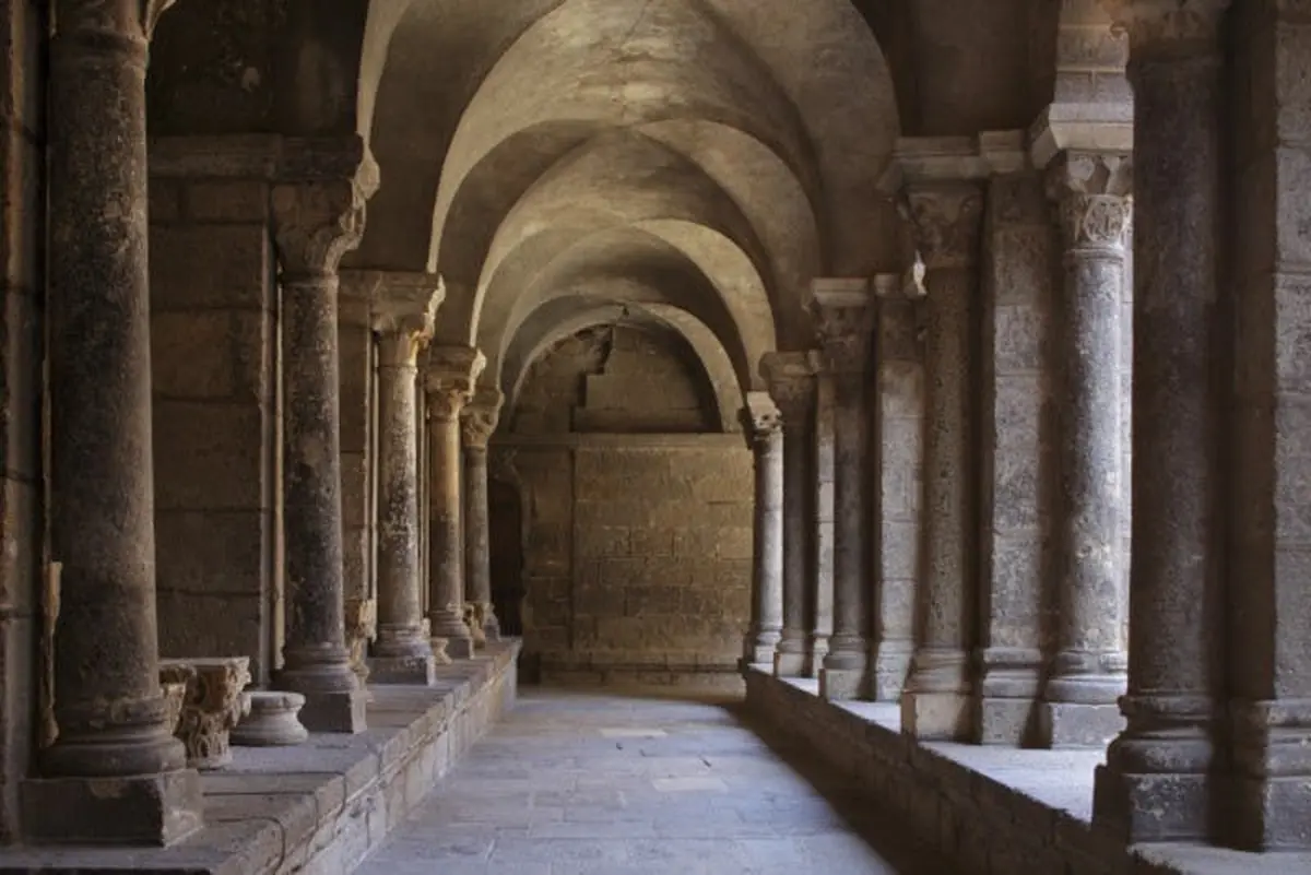 Un couloir en pierre avec des plafonds voûtés, soutenus par des colonnes, dans ce qui semble être un bâtiment ancien ou historique.