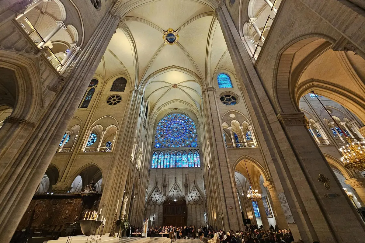 Intérieur d'une grande cathédrale avec de hauts plafonds voûtés, des vitraux, des portes cintrées et une foule de personnes rassemblées en contrebas.