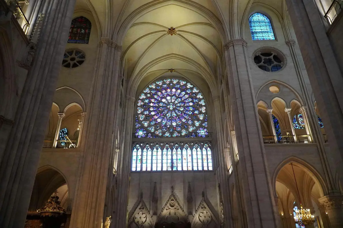Vue intérieure d'une cathédrale présentant une grande rosace en vitrail et de hauts plafonds voûtés.
