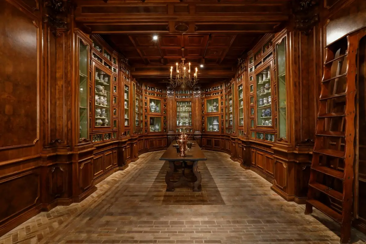 Pièce en bois ornée d'étagères de céramiques, d'une longue table, d'un sol en briques et d'un lustre suspendu au plafond.