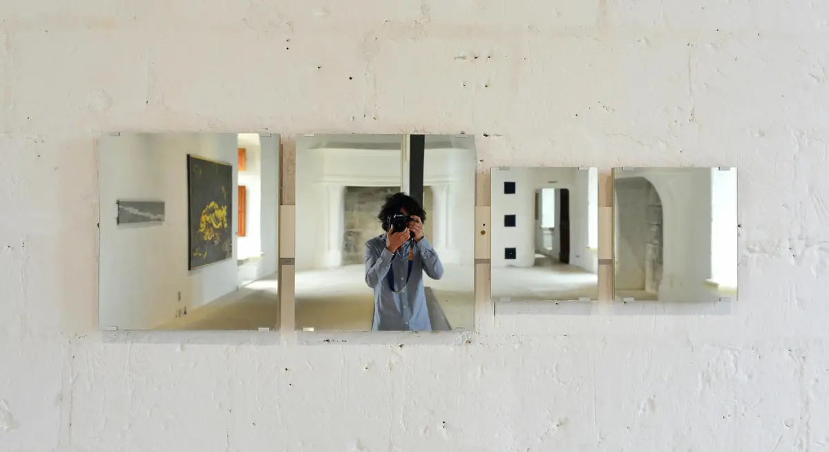 Personne se prenant en photo dans trois miroirs installés sur un mur blanc dans une galerie d'art.