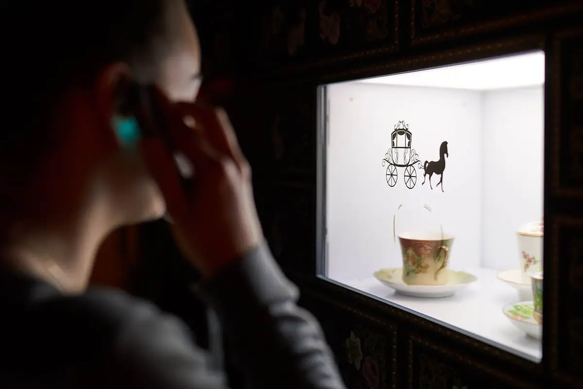 Une personne au téléphone regarde un présentoir avec une tasse à thé et une soucoupe, et une silhouette décorative d'un cheval et d'une voiture sur le verre.