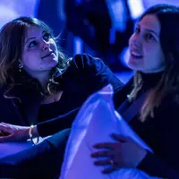 Deux femmes dans une pièce faiblement éclairée par une lumière bleue, l'une tenant un oreiller, toutes deux semblant détendues et engagées. &copy; ®Cités Immersives