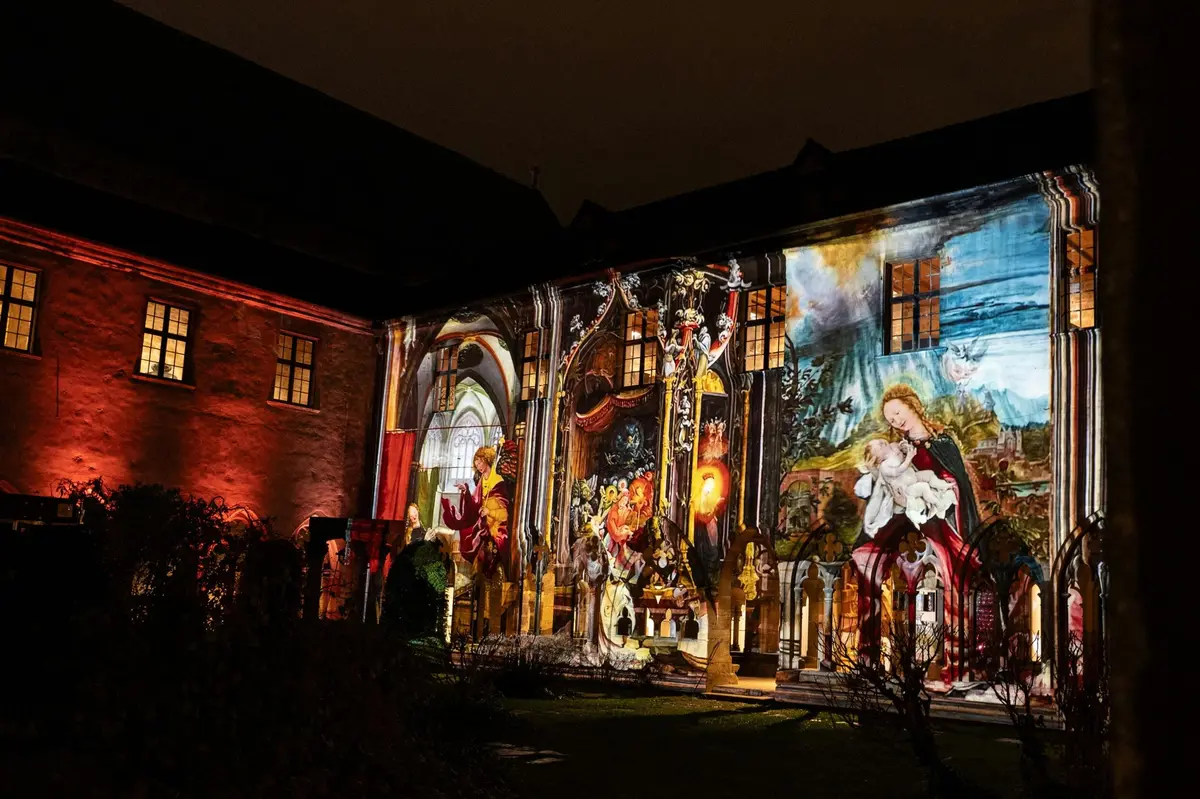 La façade d'un immeuble, éclairée la nuit par des projections artistiques colorées représentant des motifs et des personnages religieux.